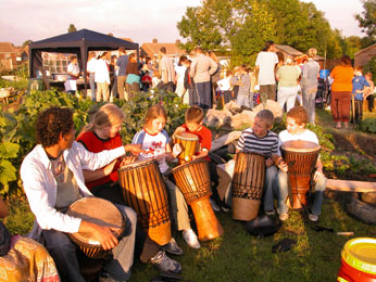 children druming on Kirk Hallam Allotments with people queing for food at gazebo in background