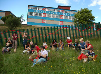 Particpants picnicing infront of railings with Interuptions ribbon, infront of building with Rowley Regis Centre text on the side
